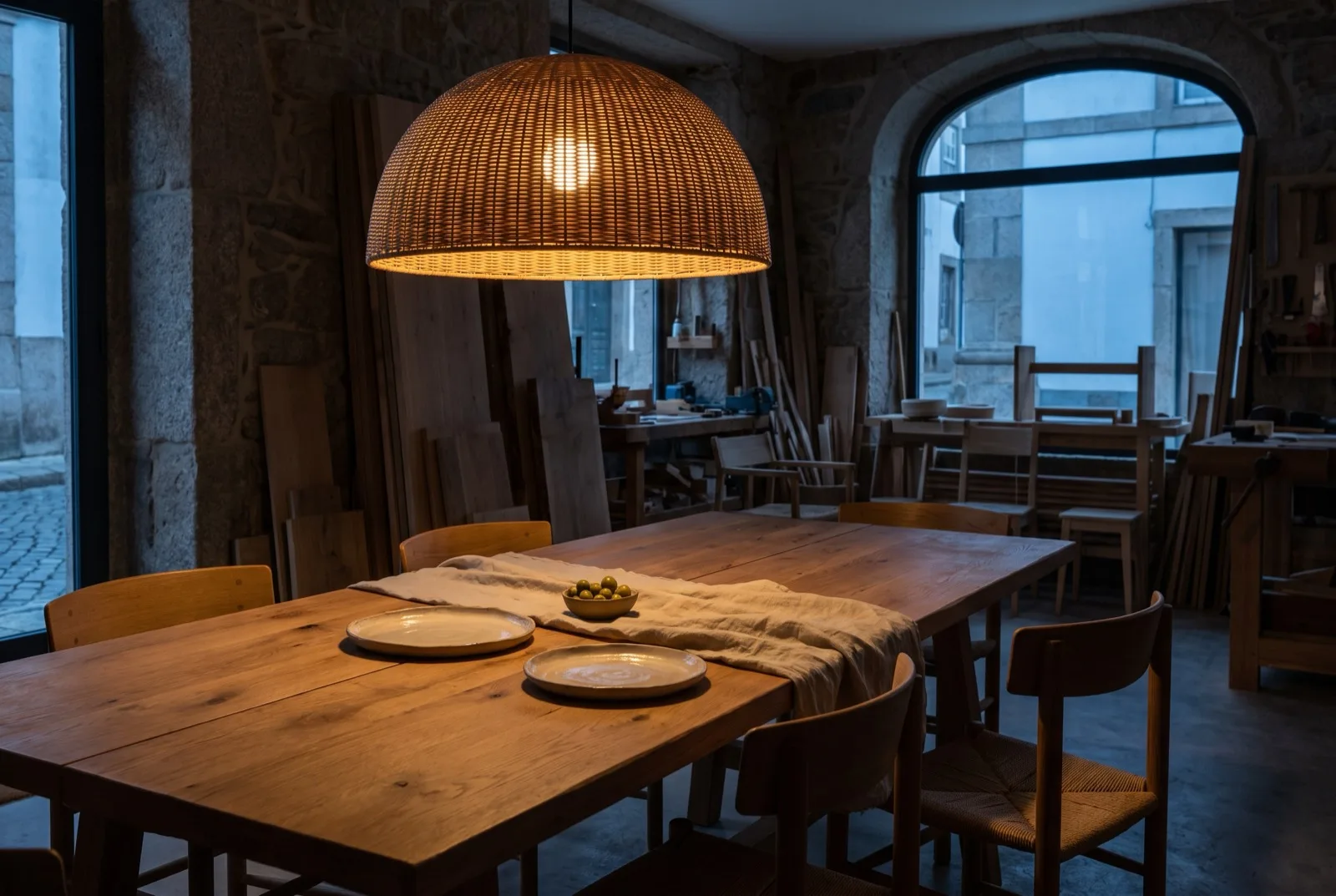 Candeeiro pendente aceso a 80 cm sobre mesa de jantar em carvalho, luz quente sobre a mesa posta ao anoitecer