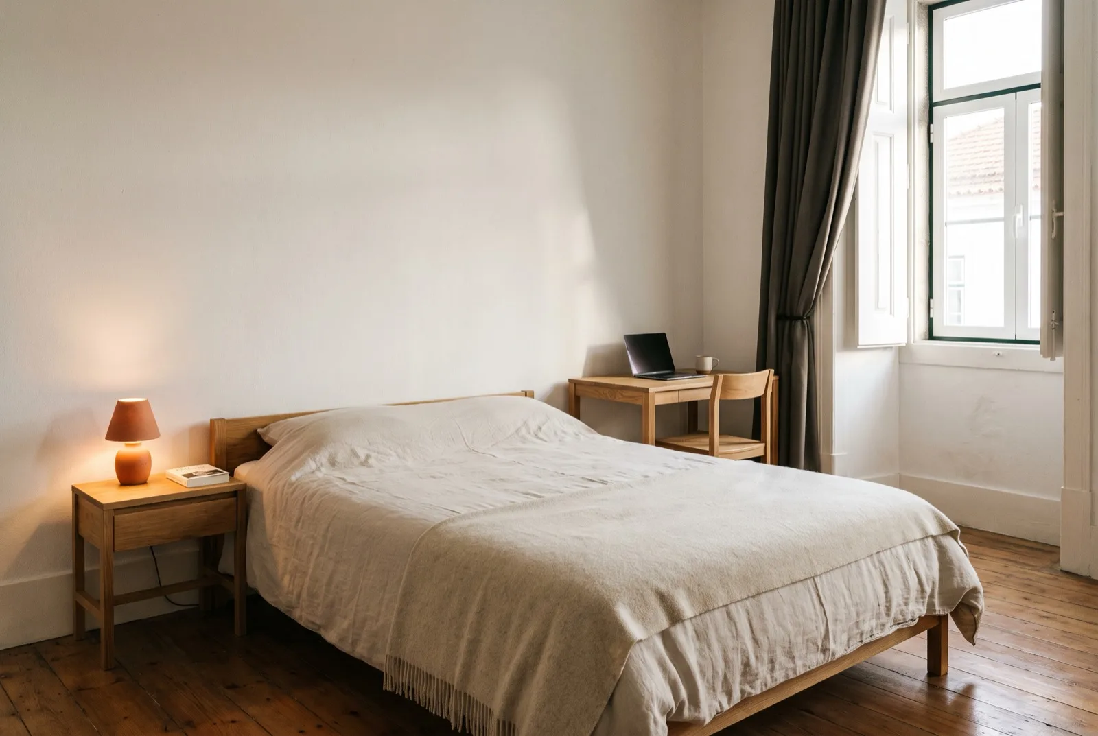 Quarto de visitas simples e digno: cama de 140 feita com roupa clara, mesinha com candeeiro e luz de manhã