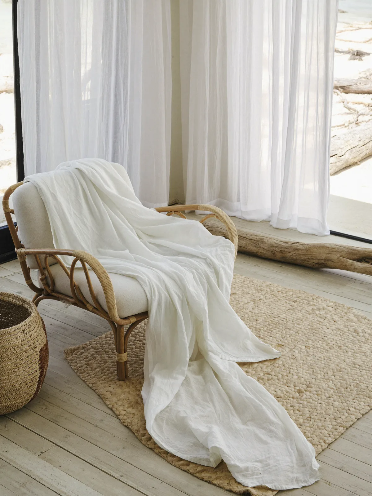 Sala costeira em estilo litoral: poltrona de rattan, tapete de juta e têxteis em branco e areia, com luz clara de praia
